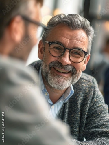 A person wearing glasses and a beard sits at a table