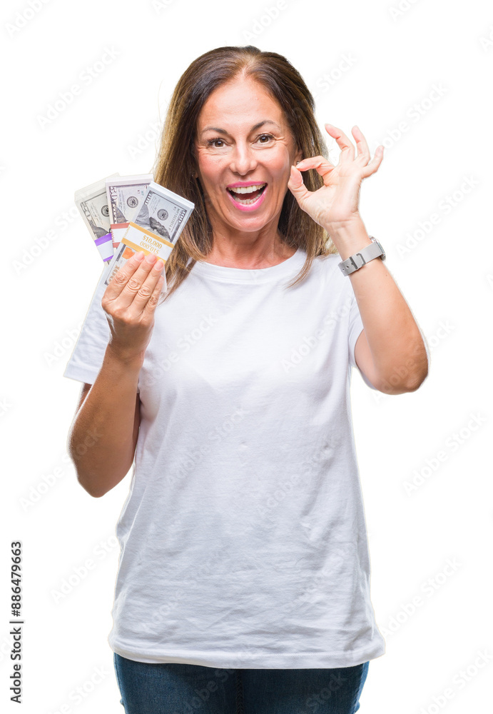 Middle age hispanic woman holding bunch of dollars over isolated background doing ok sign with fingers, excellent symbol Middle age hispanic woman holding bunch of dollars over isolated background doing ok sign with fingers, excellent symbol