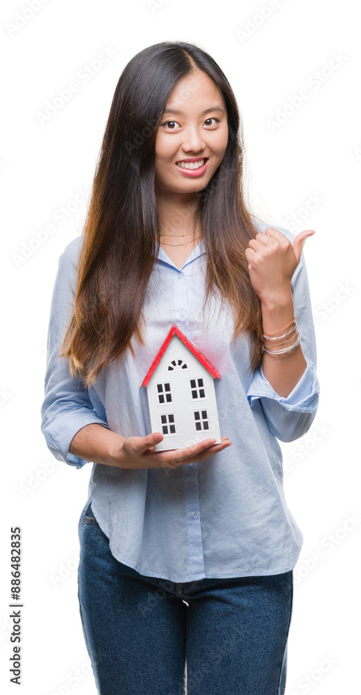 Young asian woman real state agent holding house isolated background pointing and showing with thumb up to the side with happy face smiling Young asian woman real state agent holding house isolated background pointing and showing with thumb up to the side with happy face smiling