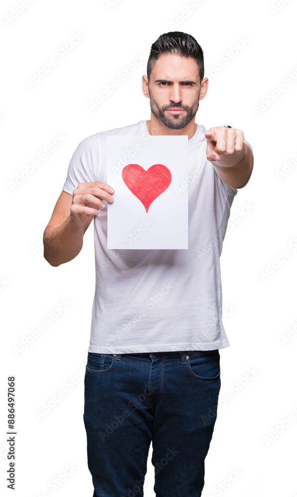 Handsome young man holding card with red heart over isolated background pointing with finger to the camera and to you, hand sign, positive and confident gesture from the front Handsome young man holding card with red heart over isolated background pointing with finger to the camera and to you, hand sign, positive and confident gesture from the front