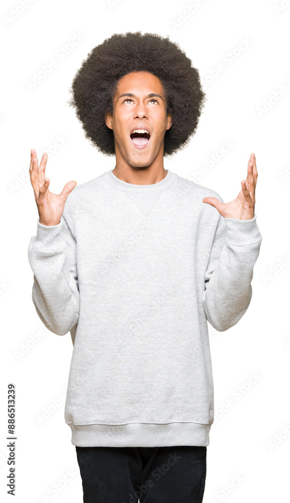 Young african american man with afro hair wearing sporty sweatshirt crazy and mad shouting and yelling with aggressive expression and arms raised. Frustration concept. Young african american man with afro hair wearing sporty sweatshirt crazy and mad shouting and yelling with aggressive expression and arms raised. Frustration concept.