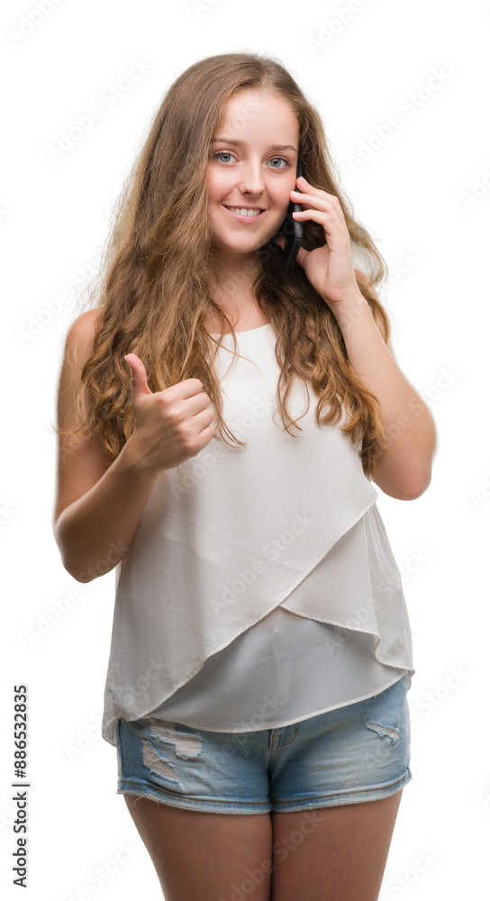 Young blonde woman using smartphone happy with big smile doing ok sign, thumb up with fingers, excellent sign Young blonde woman using smartphone happy with big smile doing ok sign, thumb up with fingers, excellent sign