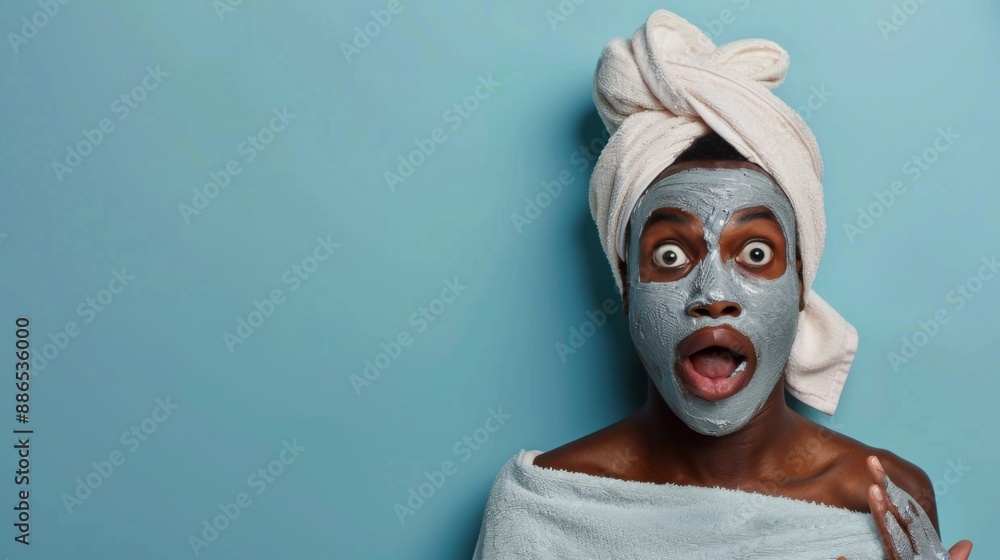 African American shocked man with clay facial mask and towel on head uses beauty products and cosmetic on blue studio background. Copy paste empty place for text. Skin care and peeling concept African American shocked man with clay facial mask and towel on head uses beauty products and cosmetic on blue studio background. Copy paste empty place for text. Skin care and peeling concept