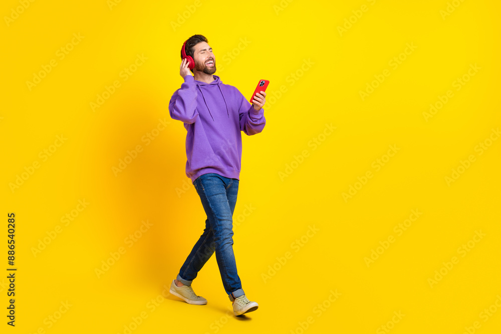 Full size photo of handsome young guy walk headphones device wear trendy violet outfit isolated on yellow color background Full size photo of handsome young guy walk headphones device wear trendy violet outfit isolated on yellow color background