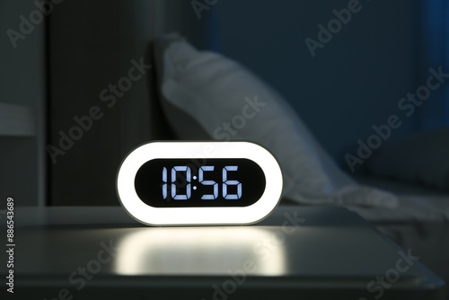 Digital alarm clock on bedside table in bedroom at night