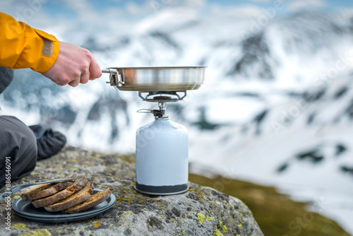 A woman's hand holds camping fry pan on a tourist gas stove to prepare food on a camping trip in the mountains photo