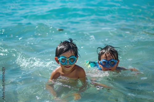 Two young children with swimming goggles are swimming happily in clear blue beach water, showcasing their joy and enthusiasm for an aquatic adventure on a sunny day. © Milos