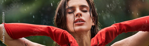 Принти на полотні A young woman in a red long gloves stands confidently, hands on hips, embracing the rain