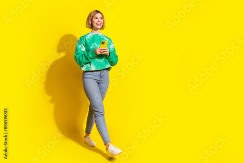 Full length photo of cheerful pretty lady dressed green sweatshirt reading modern gadget walking empty space isolated yellow color background