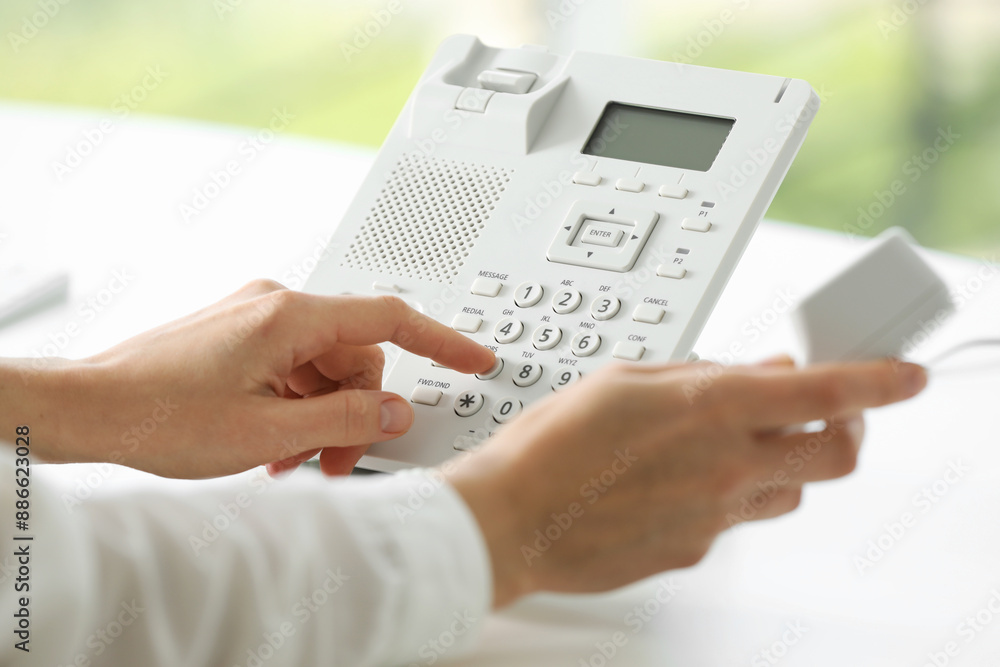 Assistant dialing number on telephone against blurred background, closeup