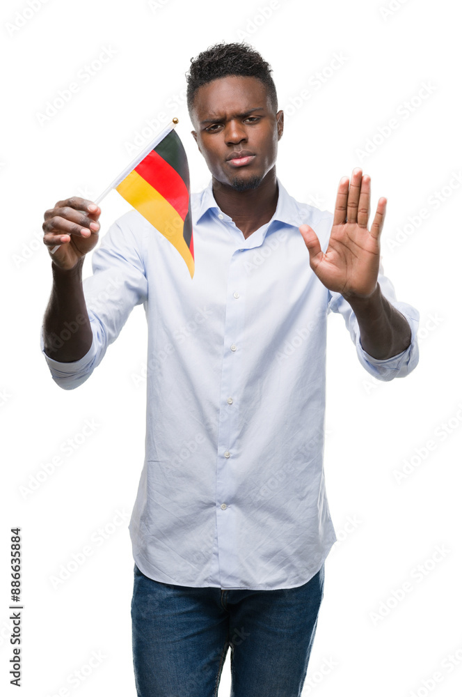 Young african american man holding german flag with open hand doing stop sign with serious and confident expression, defense gesture Young african american man holding german flag with open hand doing stop sign with serious and confident expression, defense gesture