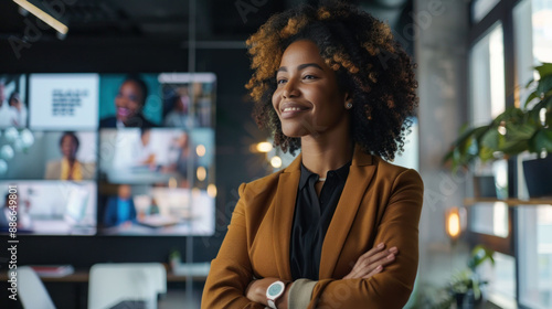 A smiling woman standing in an office and looking at a video wall, depicting a collaborative and technologically advanced work environment. photo