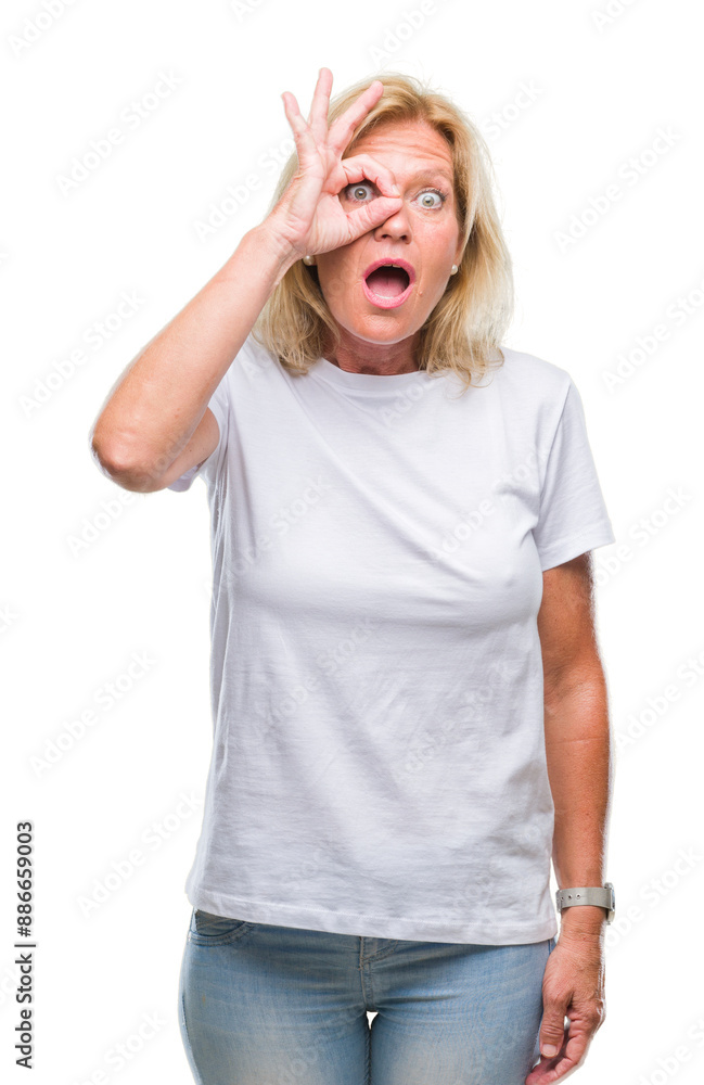 Fototapeta premium Middle age blonde woman over isolated background doing ok gesture shocked with surprised face, eye looking through fingers. Unbelieving expression.