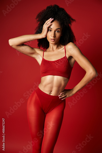 A young woman gracefully poses in a red top and tights against a vibrant background in a studio setting.