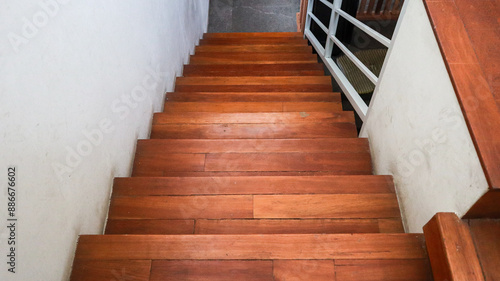 Close-up view of contrast modern wooden staircase with a white handrail. The staircase is lit by natural light, creating a bright and clean atmosphere. Wooden Staircase Interior Design