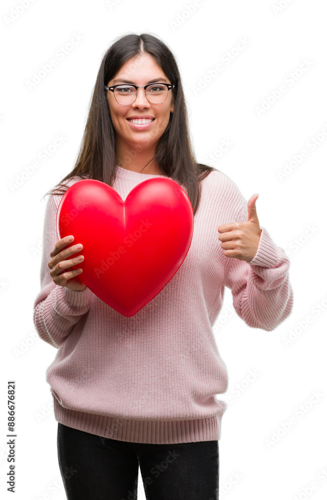 Young hispanic woman holding heart in love happy with big smile doing ok sign, thumb up with fingers, excellent sign Young hispanic woman holding heart in love happy with big smile doing ok sign, thumb up with fingers, excellent sign