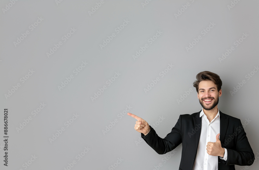 Smiling businessman pointing on light grey background. Young businessman in a grey suit and white shirt, smiling and pointing to the side on a grey background Smiling businessman pointing on light grey background. Young businessman in a grey suit and white shirt, smiling and pointing to the side on a grey background