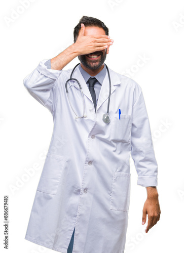 Adult hispanic doctor man over isolated background smiling and laughing with hand on face covering eyes for surprise. Blind concept.