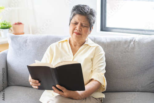 Quadro em tela Presbyopia, Hyperopia mature, aged asian woman having vision problem trying to stare read text on a book on sofa at home, eye disease of elderly