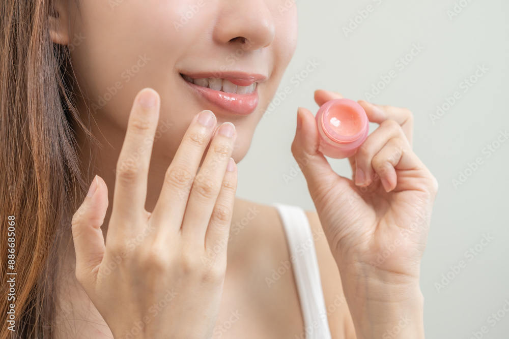 Lip care protection concept, asian young woman, girl applying balm from jar, taking with finger, touching on dry mouth from natural beauty product, skincare routine, makeup and cosmetics on background Lip care protection concept, asian young woman, girl applying balm from jar, taking with finger, touching on dry mouth from natural beauty product, skincare routine, makeup and cosmetics on background