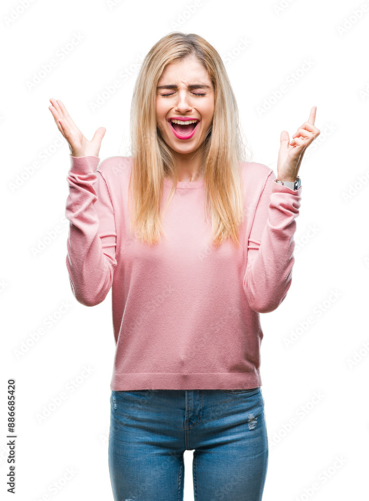 Young beautiful blonde woman wearing pink winter sweater over isolated background celebrating mad and crazy for success with arms raised and closed eyes screaming excited. Winner concept Young beautiful blonde woman wearing pink winter sweater over isolated background celebrating mad and crazy for success with arms raised and closed eyes screaming excited. Winner concept