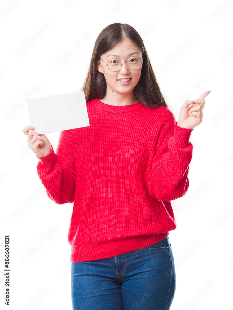 Young Chinese woman over isolated background holding blank card very happy pointing with hand and finger to the side Young Chinese woman over isolated background holding blank card very happy pointing with hand and finger to the side