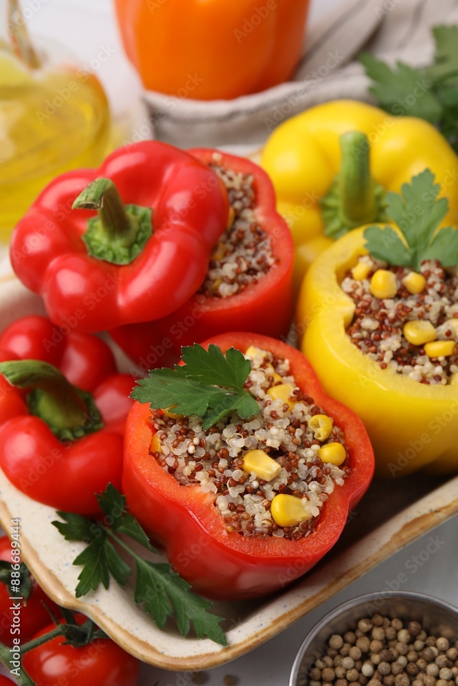 Quinoa stuffed bell peppers in baking dish, parsley, tomatoes and peppercorns on white table, closeup Quinoa stuffed bell peppers in baking dish, parsley, tomatoes and peppercorns on white table, closeup