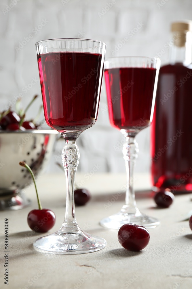 Delicious cherry liqueur in glasses and fresh berries on light grey table Delicious cherry liqueur in glasses and fresh berries on light grey table
