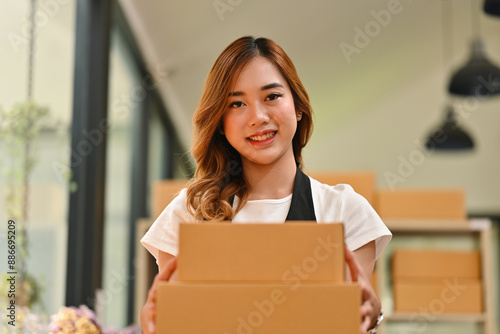 A cheerful woman holds packages ready for delivery, the positive attitude of an SME, focusing on customer satisfaction and the efficient preparation of orders for delivery