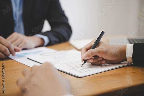 Fototapeta Naklejka Na Ścianę i Meble -  businessman sitting at desk holds pen signing contract paper, lease mortgage, employment hr or affirm partnership