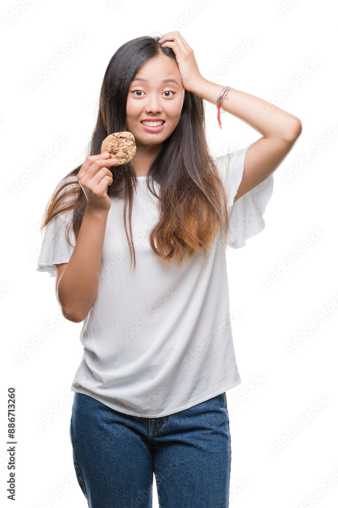 Young asian woman eating chocolate chip cookie over isolated background stressed with hand on head, shocked with shame and surprise face, angry and frustrated. Fear and upset for mistake. Young asian woman eating chocolate chip cookie over isolated background stressed with hand on head, shocked with shame and surprise face, angry and frustrated. Fear and upset for mistake.