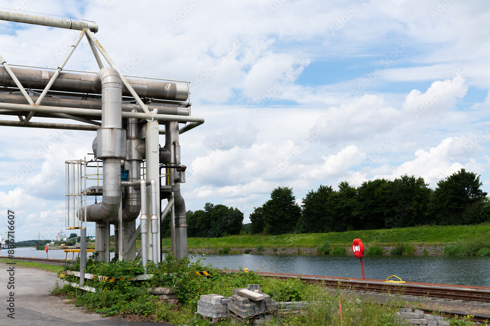A large industrial pipeline crosses a canal, with green trees and a blue sky in the background. A large industrial pipeline crosses a canal, with green trees and a blue sky in the background.