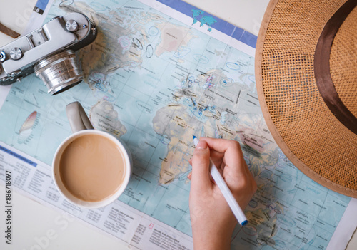 Travel planning concept. Top view of woman's hands writing on map with camera and cup of coffee