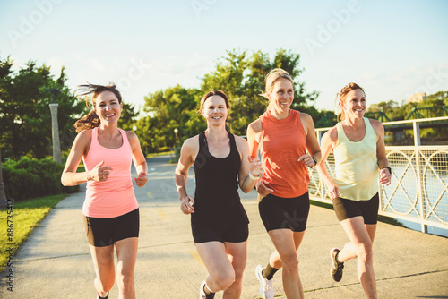 females in sportswear jogging together bright sunny park in summer © Louis-Photo