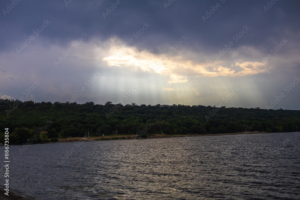 Fototapeta premium The sun's rays are reflected in the water from the river coming out from behind the rain clouds