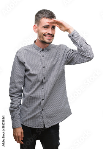 Young hipster man very happy and smiling looking far away with hand over head. Searching concept.