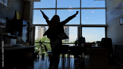 Silhouette of person with raised arms in office moment of triumph and success career achievement. Person silhouette with arms raised high in office signifies victorious moment of success career.