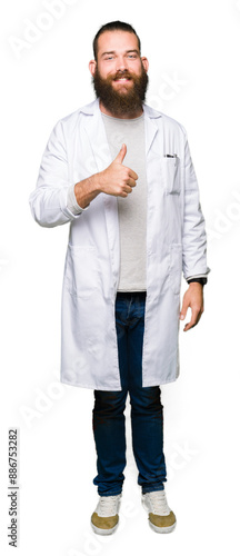 Young blond scientist man wearing white coat doing happy thumbs up gesture with hand. Approving expression looking at the camera with showing success.