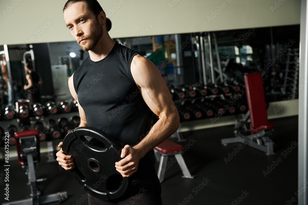 An athletic man in active wear holding a black plate in a gym. An athletic man in active wear holding a black plate in a gym.
