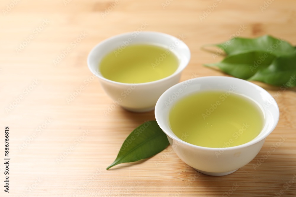 Refreshing green tea in cups and leaves on wooden table, closeup Refreshing green tea in cups and leaves on wooden table, closeup