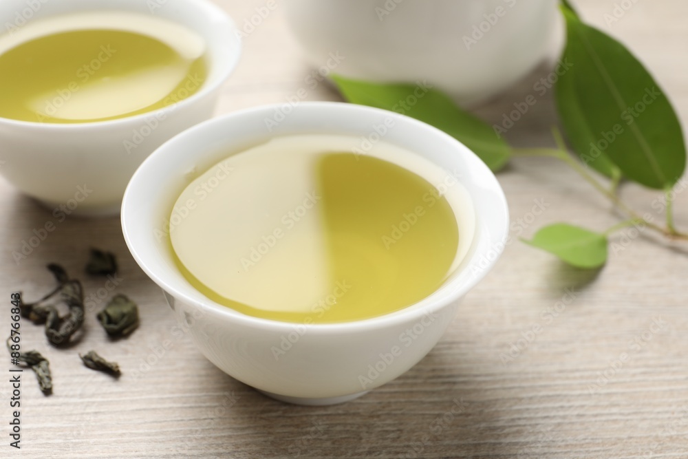 Refreshing green tea in cups and leaves on wooden table, closeup Refreshing green tea in cups and leaves on wooden table, closeup