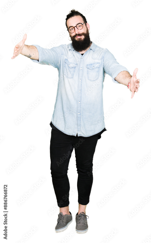 Young hipster man with long hair and beard wearing glasses looking at the camera smiling with open arms for hug. Cheerful expression embracing happiness. Young hipster man with long hair and beard wearing glasses looking at the camera smiling with open arms for hug. Cheerful expression embracing happiness.