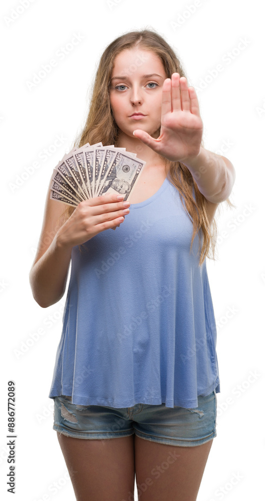 Young blonde woman holding dollars with open hand doing stop sign with serious and confident expression, defense gesture Young blonde woman holding dollars with open hand doing stop sign with serious and confident expression, defense gesture