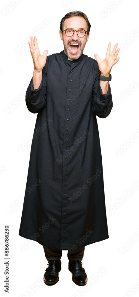 Middle age priest man wearing catholic robe celebrating crazy and amazed for success with arms raised and open eyes screaming excited. Winner concept