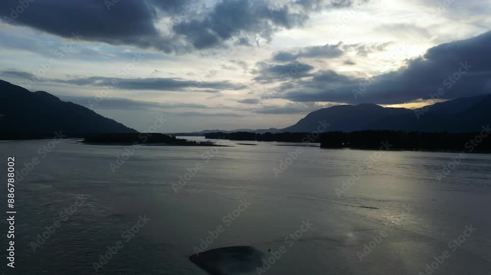 Scenic River and Mountain Landscape at Sunset. Summer season. Dramatic Cloudy Sky. Fraser River, British Columbia, Canada. Scenic River and Mountain Landscape at Sunset. Summer season. Dramatic Cloudy Sky. Fraser River, British Columbia, Canada.