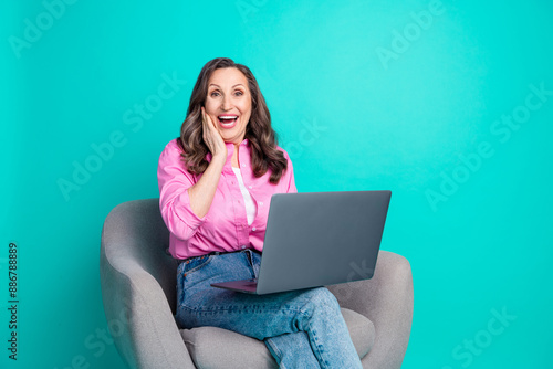 Photo of adorable excited woman wear pink shirt sitting armchair typing modern device empty space isolated blue color background