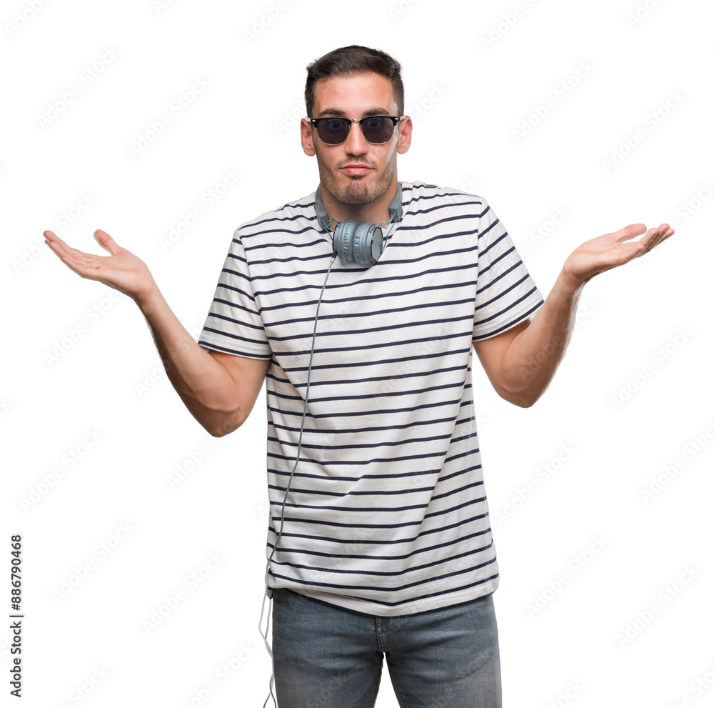 Handsome young man wearing headphones clueless and confused expression with arms and hands raised. Doubt concept. Handsome young man wearing headphones clueless and confused expression with arms and hands raised. Doubt concept.