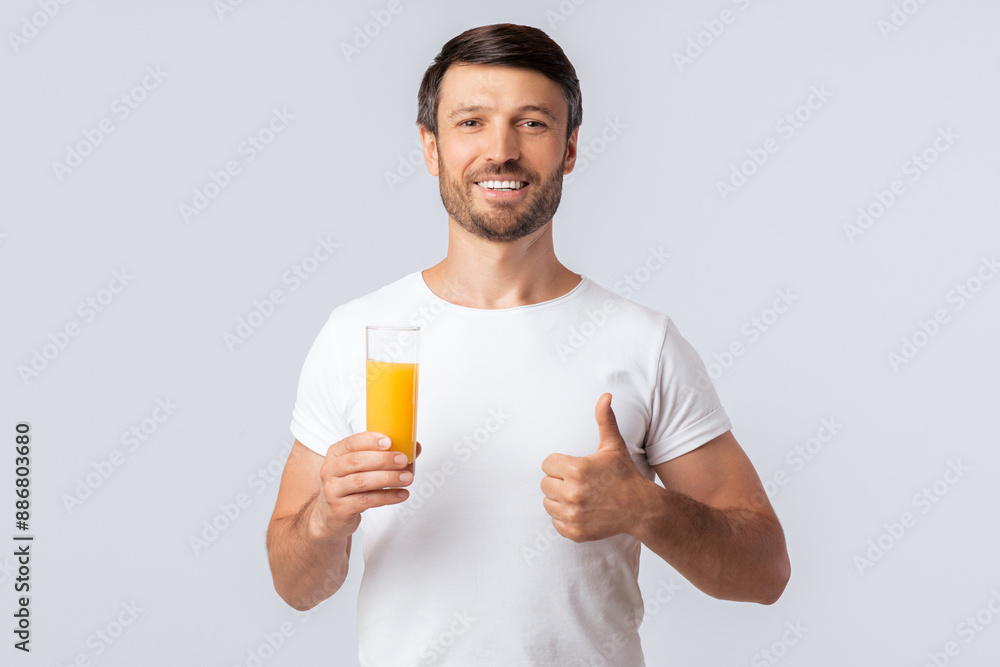 Healthy Nutrition. Cheerful Man Holding Glass Of Orange Juice Gesturing Thumbs-Up Over White Background In Studio. Free Space Healthy Nutrition. Cheerful Man Holding Glass Of Orange Juice Gesturing Thumbs-Up Over White Background In Studio. Free Space