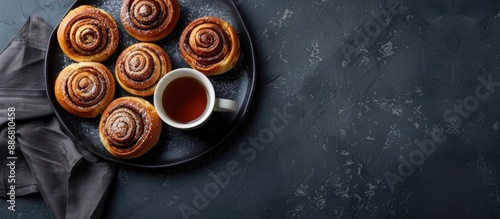 Cinnamon rolls and buns are arranged enticingly on a black plate accompanied by a cup of tea. The dark backdrop enhances the presentation with available copy space image in a top view. photo