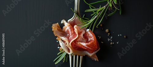 Closeup view of a fork with a delicious slice of jamon and rosemary on a black backdrop, providing space for a copy image. photo